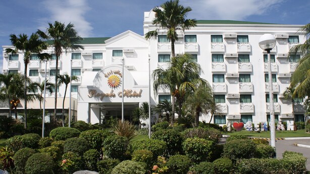 Un hotel con fachada blanca, varios balcones y un letrero central con forma de sol.