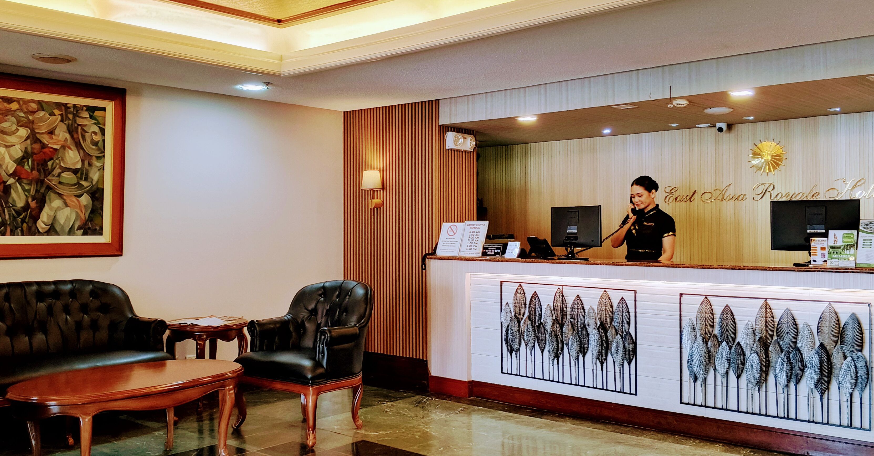A reception area with a receptionist, a black leather sofa, a wooden chair, and a wall-mounted clock.