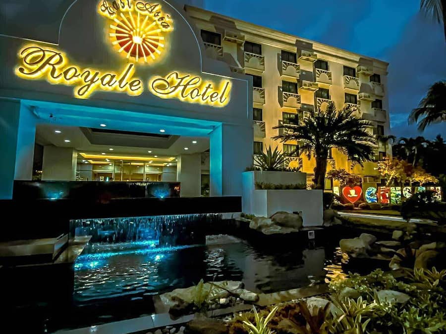 The Royale Hotel with a well-lit entrance, a water feature in front, and a view of the building's architecture.