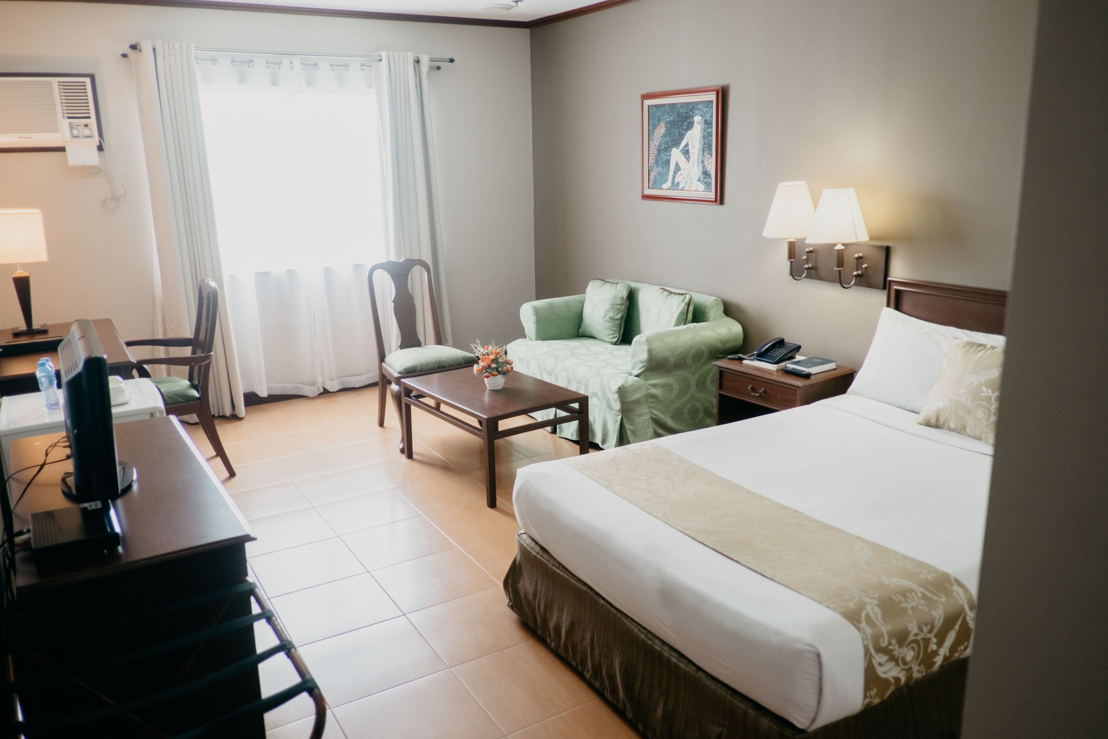 Una habitación de hotel con cama, escritorio, silla y una pequeña mesa con un jarrón.