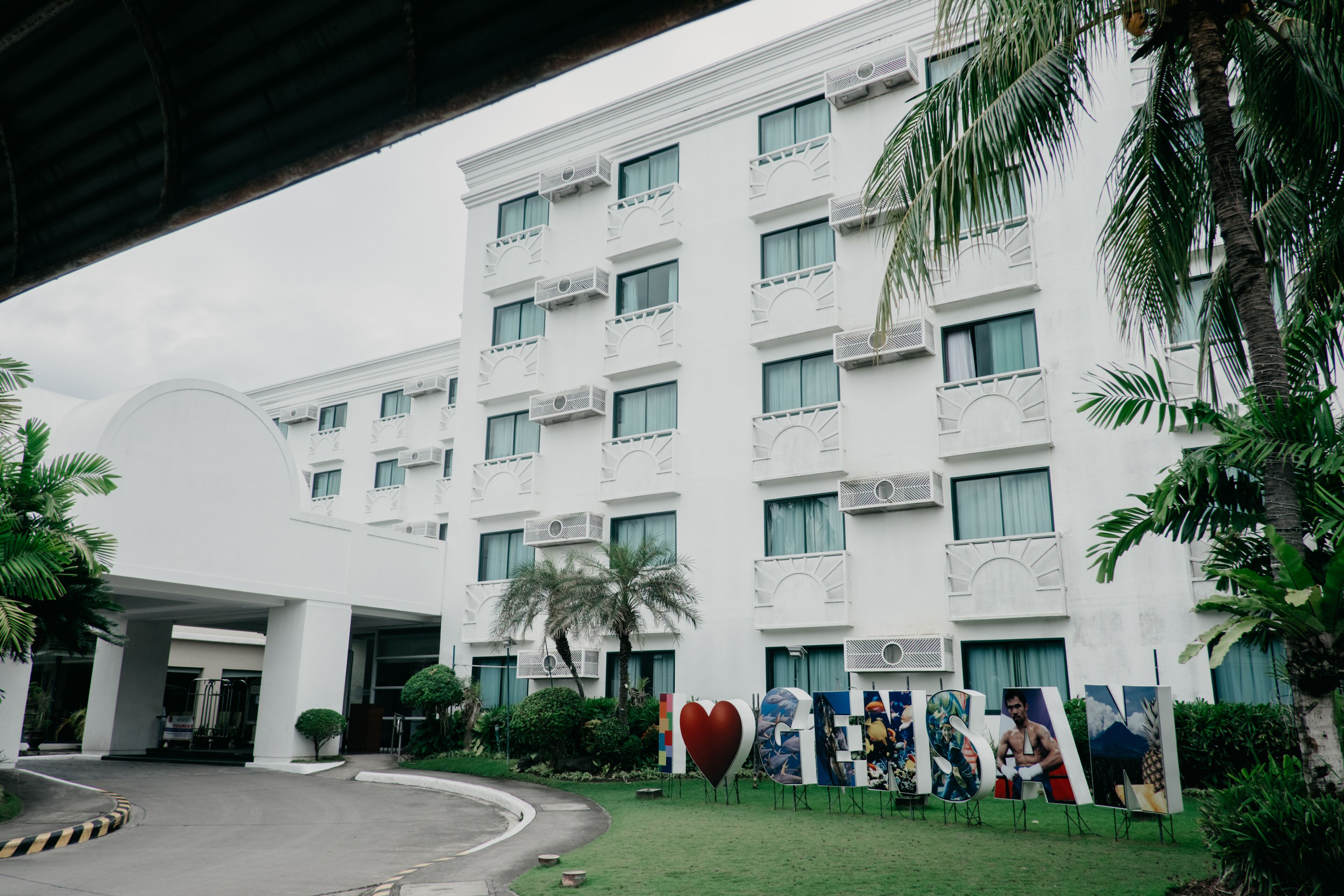 A multi-story hotel with a white facade, balconies, and a covered entrance.