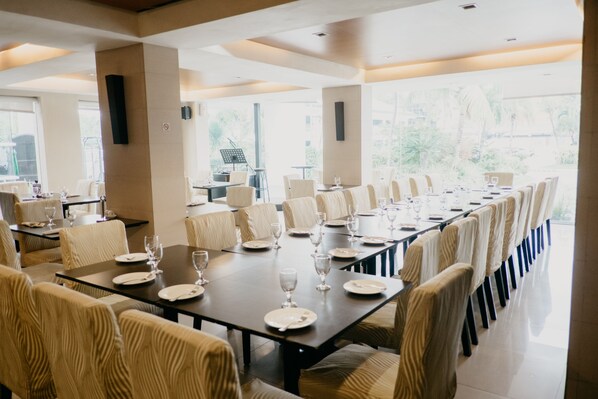 A spacious dining area with long tables and chairs, large windows, and a view of the outdoors.