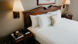 Una cama bien hecha con sábanas blancas y un cabecero de madera, flanqueada por dos mesitas de noche con lámparas y un teléfono.