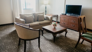 Una habitación de hotel con sofá, sillón, mesa de centro, televisor y cómoda.