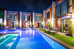Ein modernes Hotel mit Pool, Liegestühlen und einer gut beleuchteten Außenansicht bei Nacht.