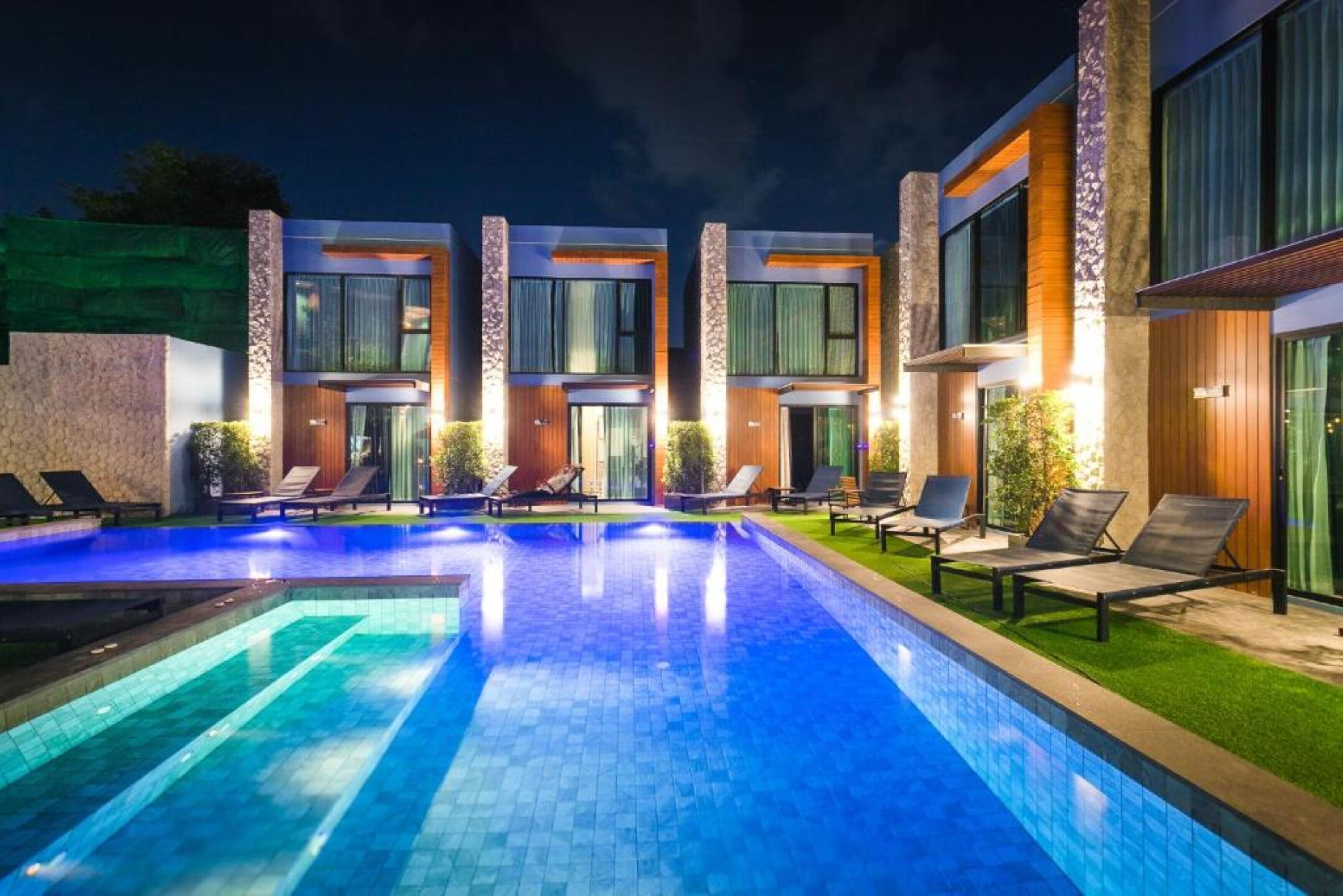 A modern hotel with a swimming pool, lounge chairs, and a well-lit exterior.