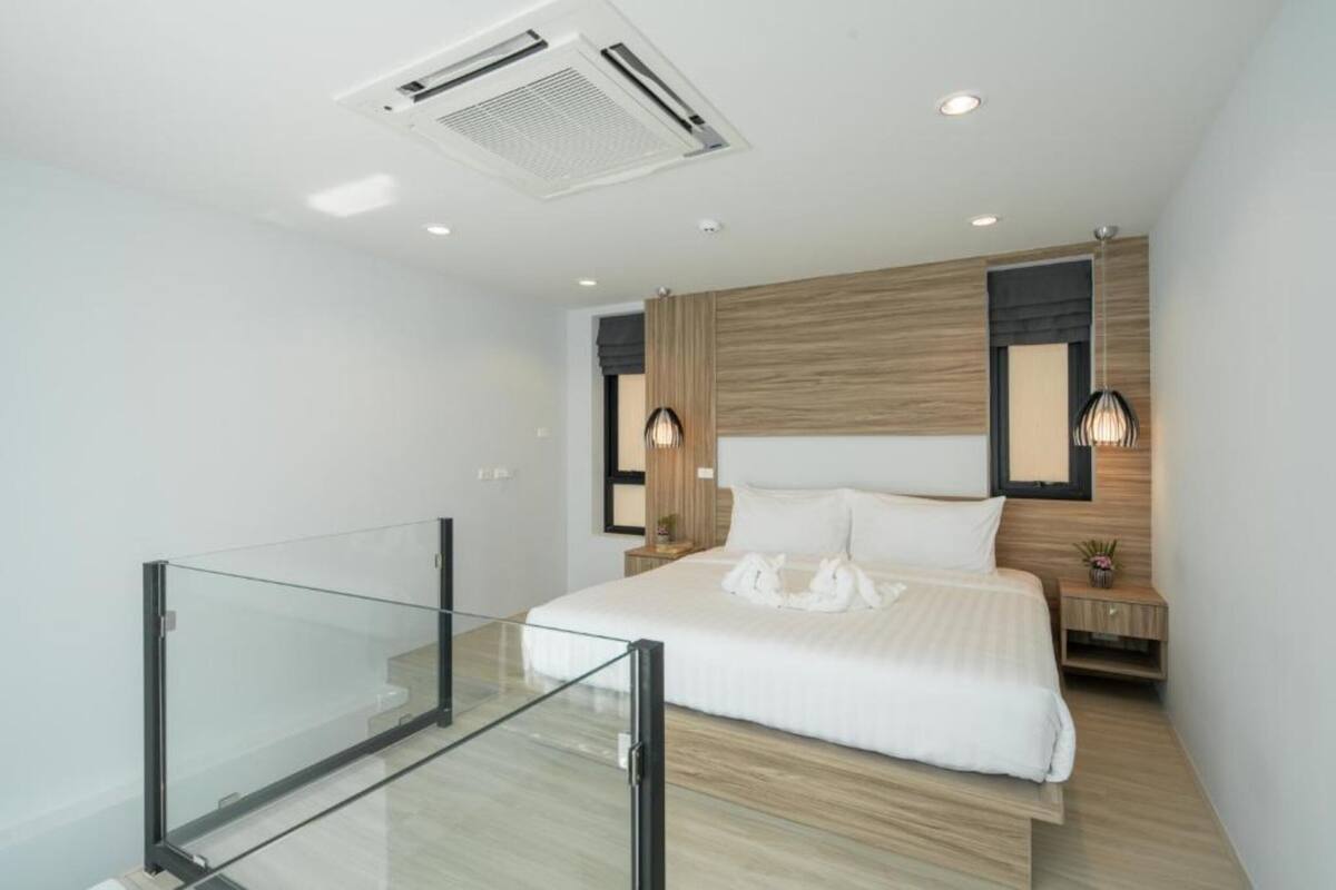 Ein modernes Schlafzimmer mit Glastrennwand, einem großen Bett, einem Holz-Kopfteil und zwei Nachttischlampen.