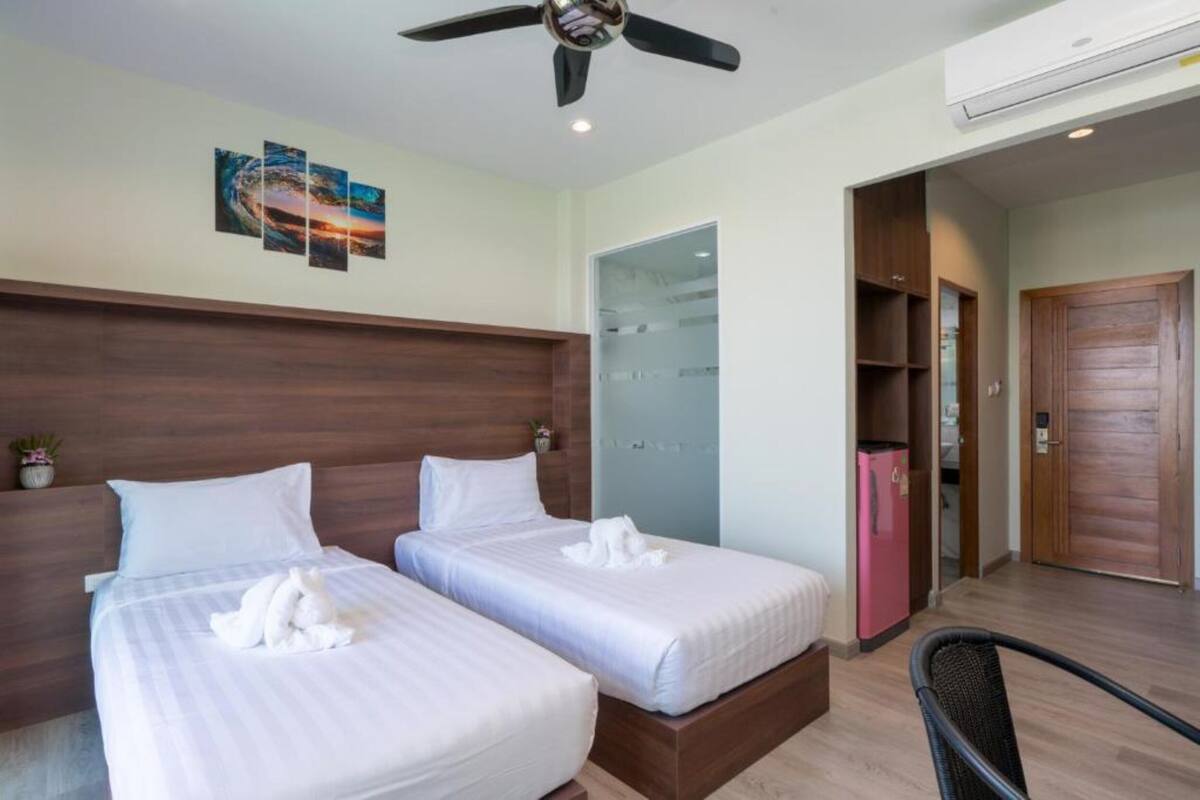 Ein Hotelzimmer mit zwei Betten, einem Deckenventilator, einer Wandklimaanlage und einer Tür zu einem Schrank.