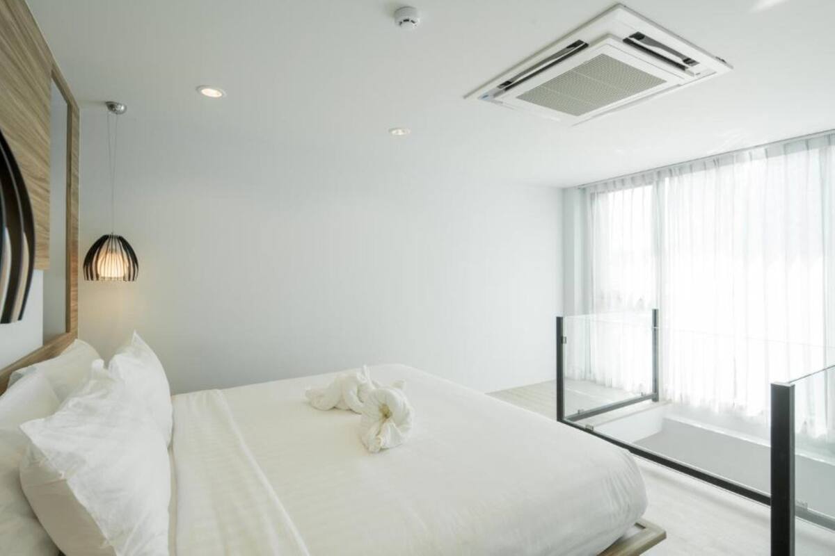 Ein Hotelzimmer mit einem großen Bett, einem Nachttisch, einer Wand-Klimaanlage und einem Fenster mit transparenten Vorhängen.