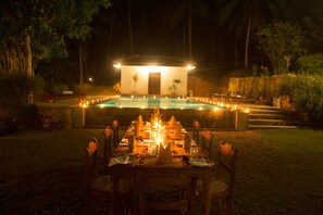 An outdoor dining area with a pool, surrounded by a stone wall and vegetation. - Thalpe Walawwa Heritage Villa (Unawatuna)