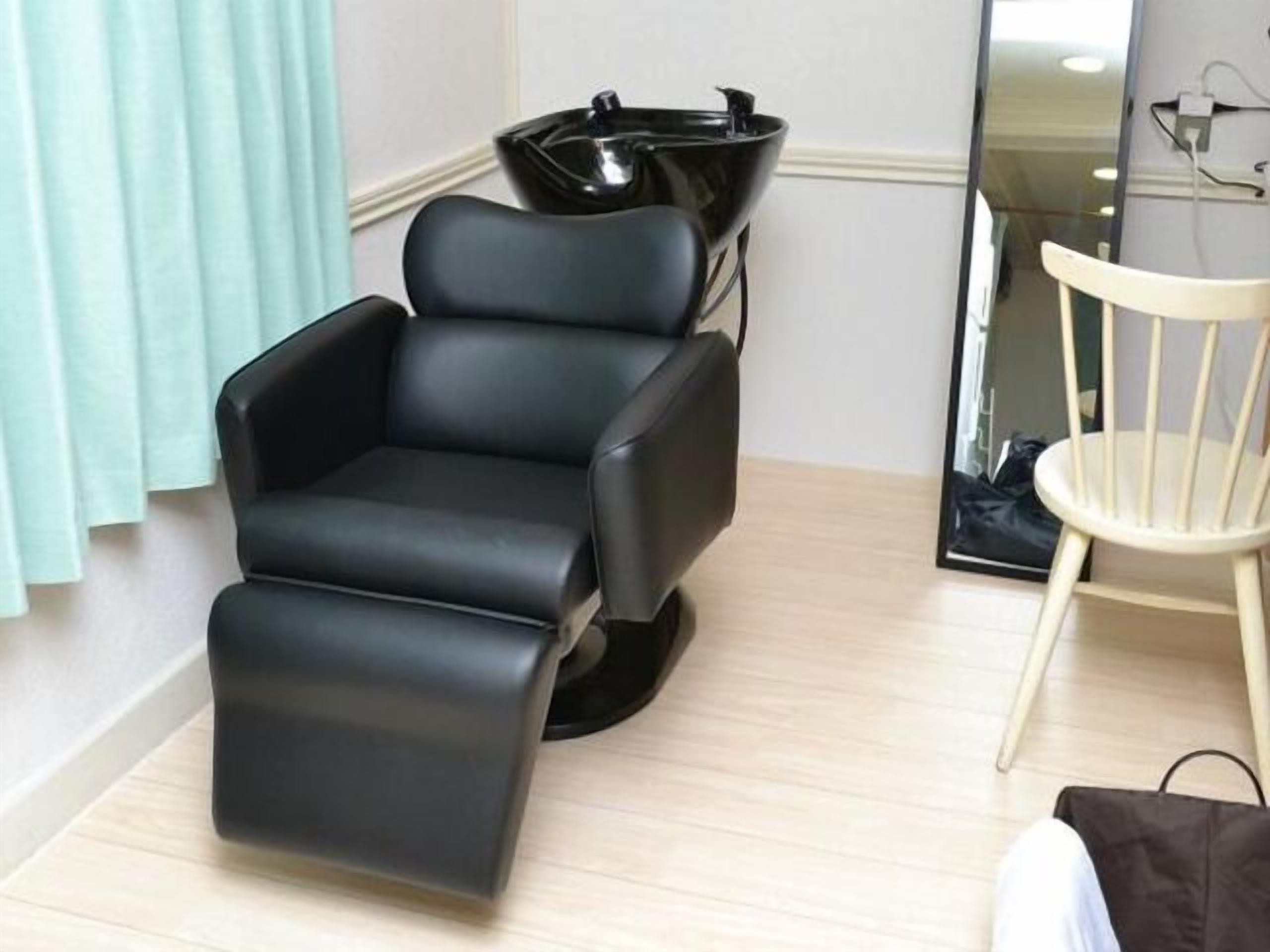 Une pièce comprenant un fauteuil de massage noir, une chaise blanche et un lavabo noir.