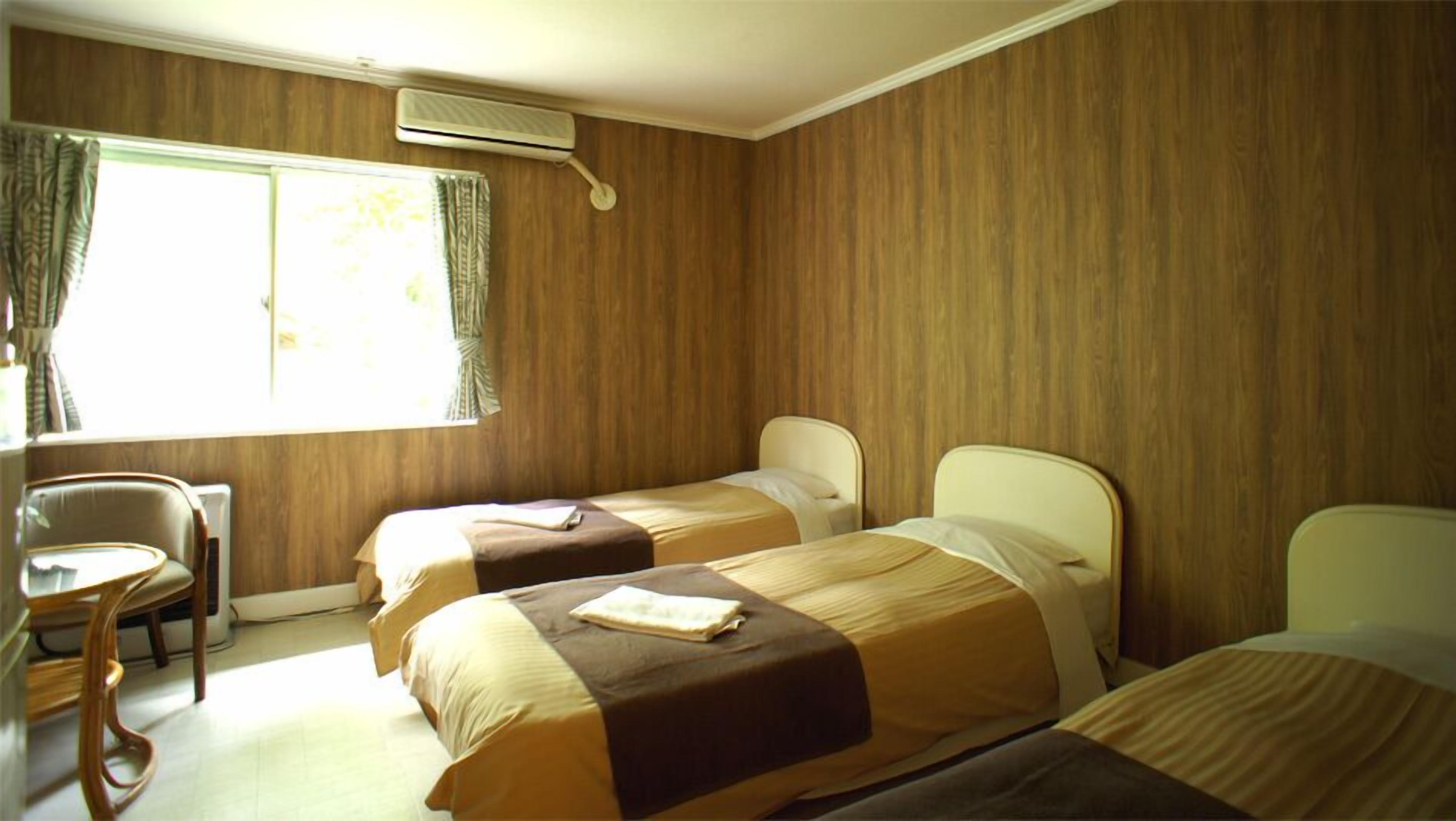 Una habitación con dos camas, una silla y un ventanal con cortinas.