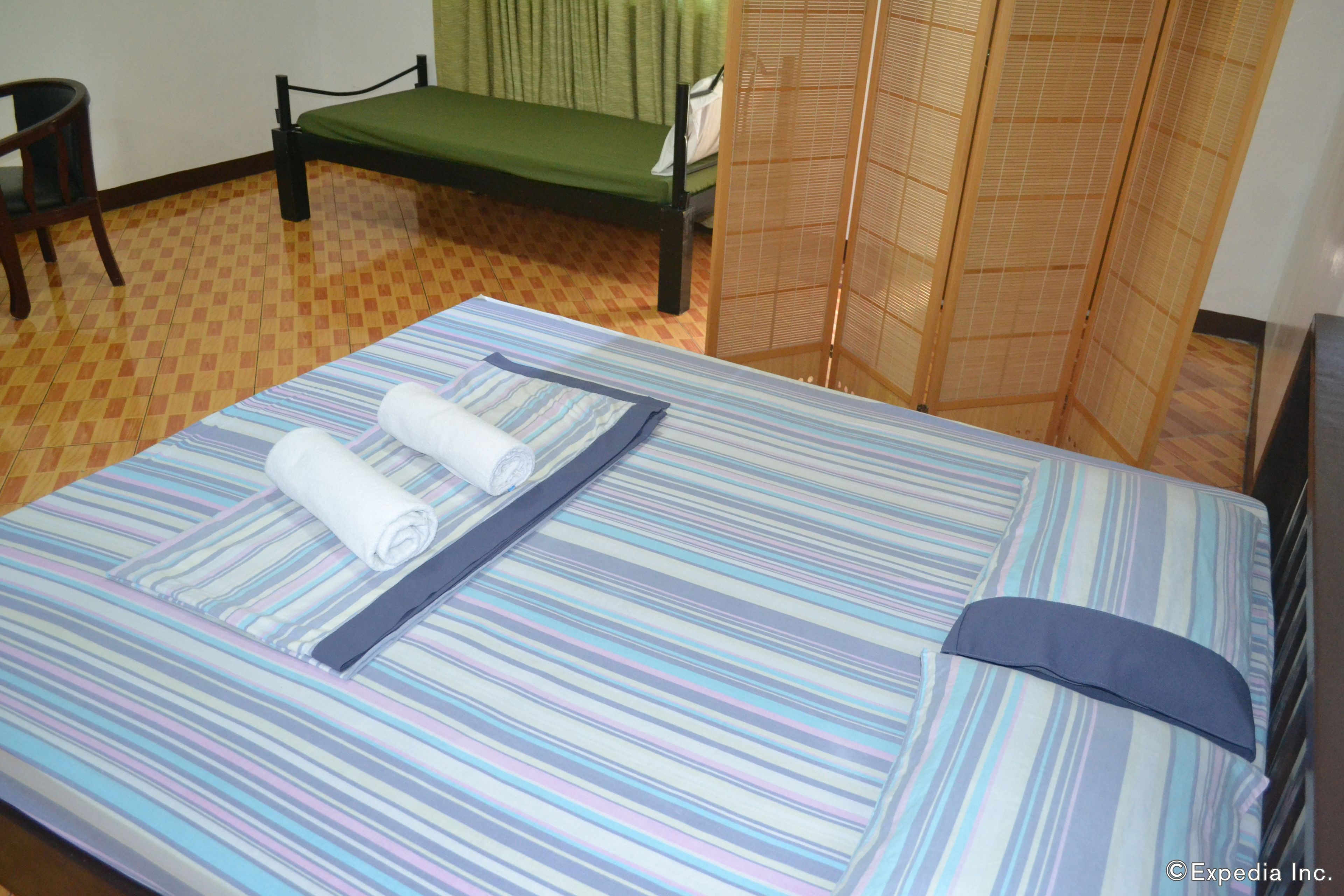 Uma cama bem arrumada com roupa de cama listrada, um sofá verde e uma divisória de madeira.