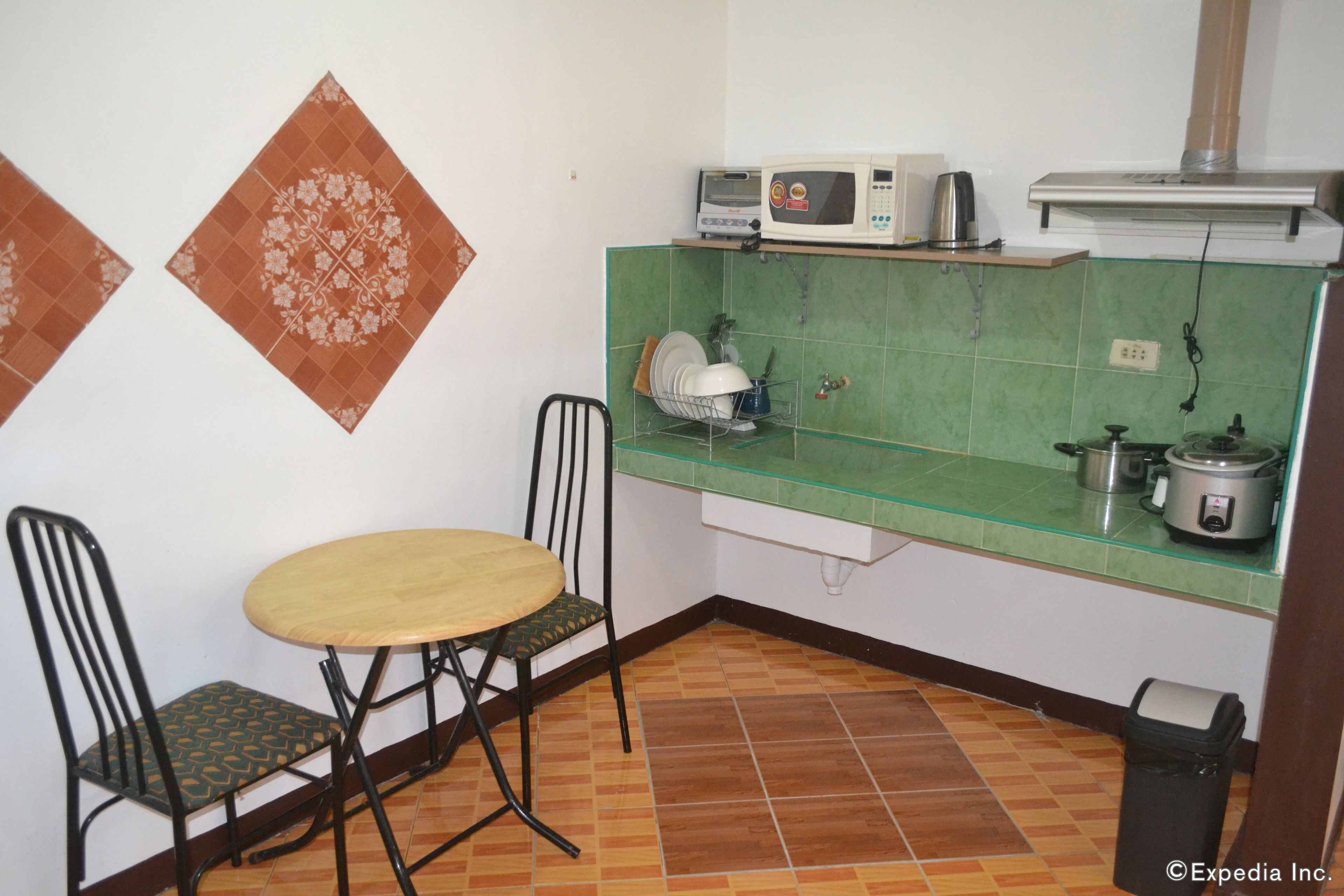 A small kitchen with a round table and two chairs, a microwave, a kettle, and a slow cooker on the counter.