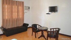 A living room with a sofa, two chairs, a small table, a TV mounted on the wall, and an air conditioning unit. - Antonio's Apartelle & Suites (General Santos)