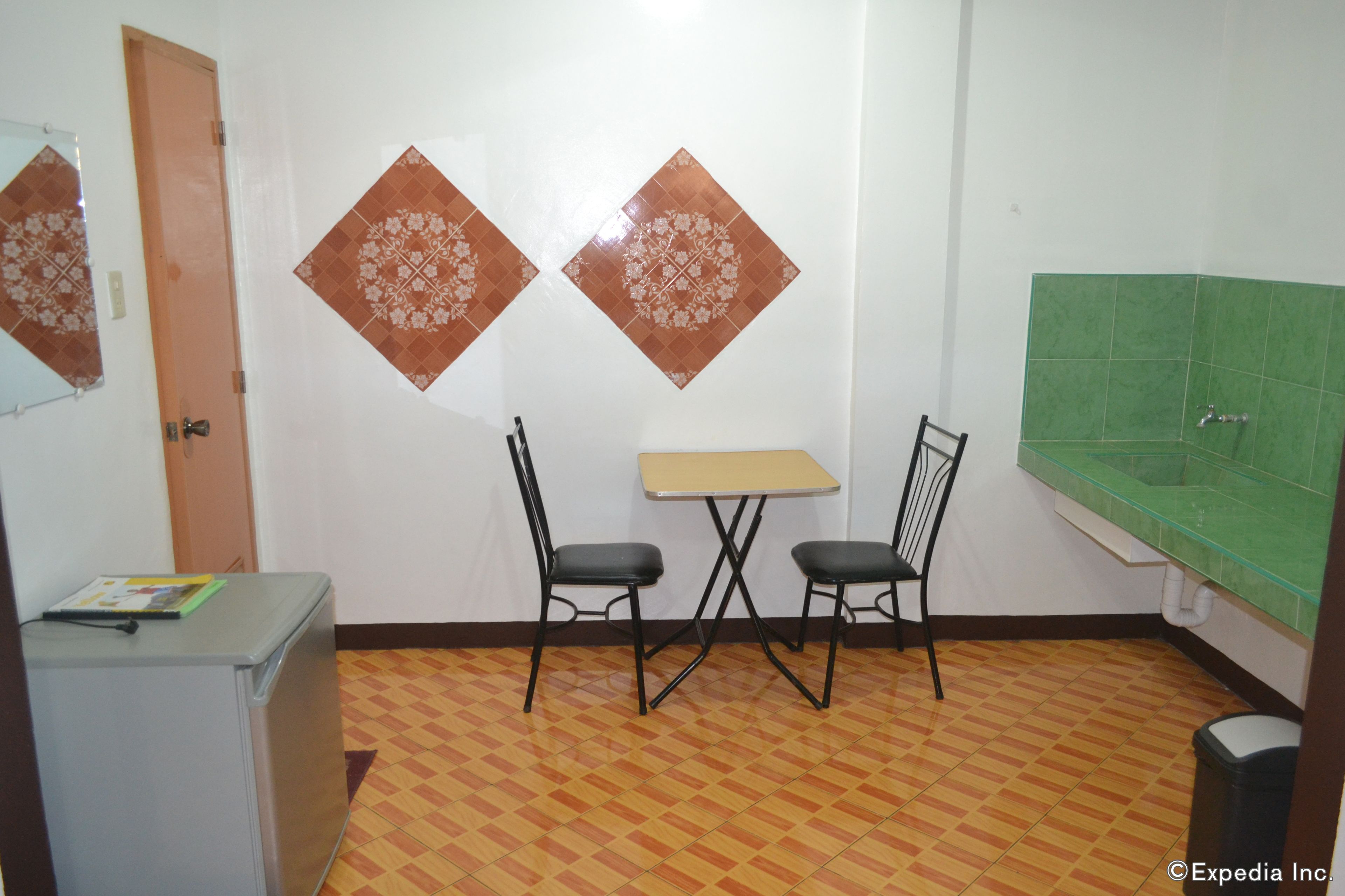 A small room with a table and two chairs, a refrigerator, and a green tiled wall.