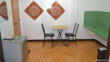 A small room with a table and two chairs, a refrigerator, and a green tiled wall.