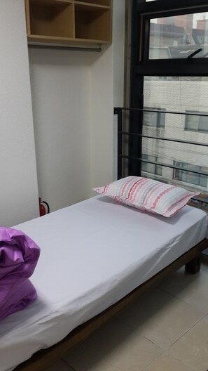 A single bed with a white mattress and a striped pillow, a wooden headboard, a small shelf, and a window with a view of buildings. - Solo Residence in Central (Seoul)