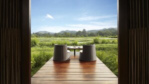 A wooden deck with two wicker chairs facing a lush green landscape with terraced fields and distant hills. - Jetwing Kaduruketha (Wellawaya)