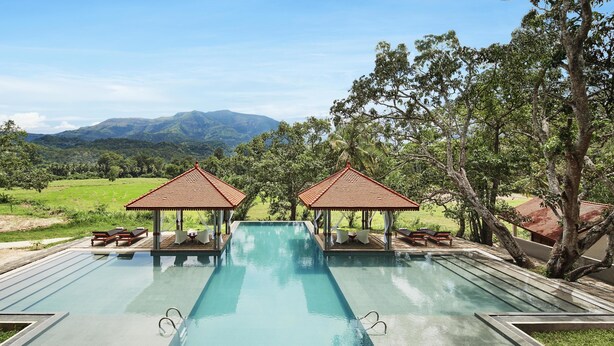 A swimming pool with two gazebos, lounge chairs, and a view of mountains. - Jetwing Kaduruketha (Wellawaya)