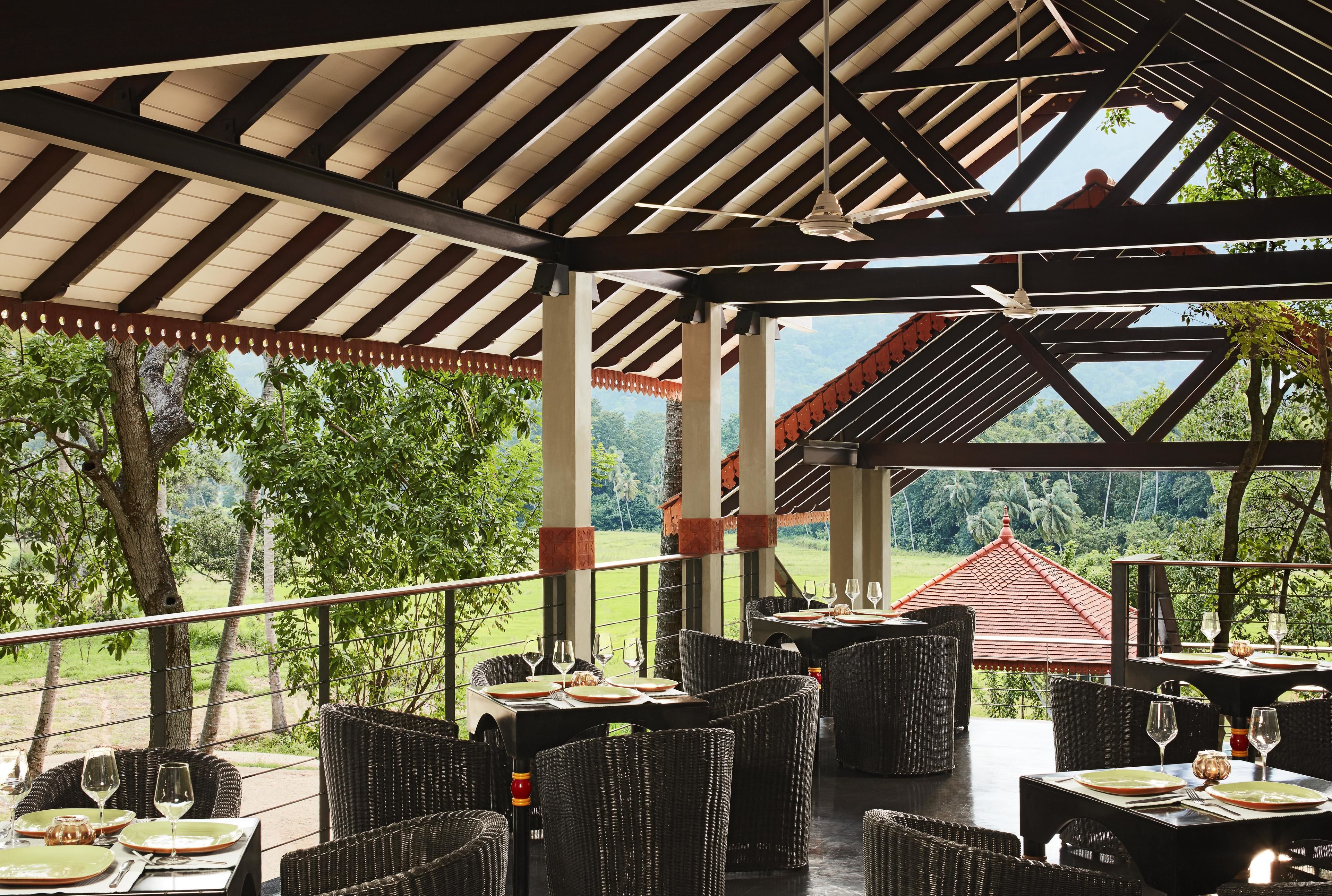 Un área de comedor al aire libre con mobiliario de mimbre y mesas dispuestas para una comida, con vistas a un paisaje pintoresco.