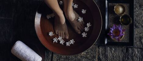 A wooden basin with water and white flowers, a purple lotus flower, and two small bowls on a stone floor.