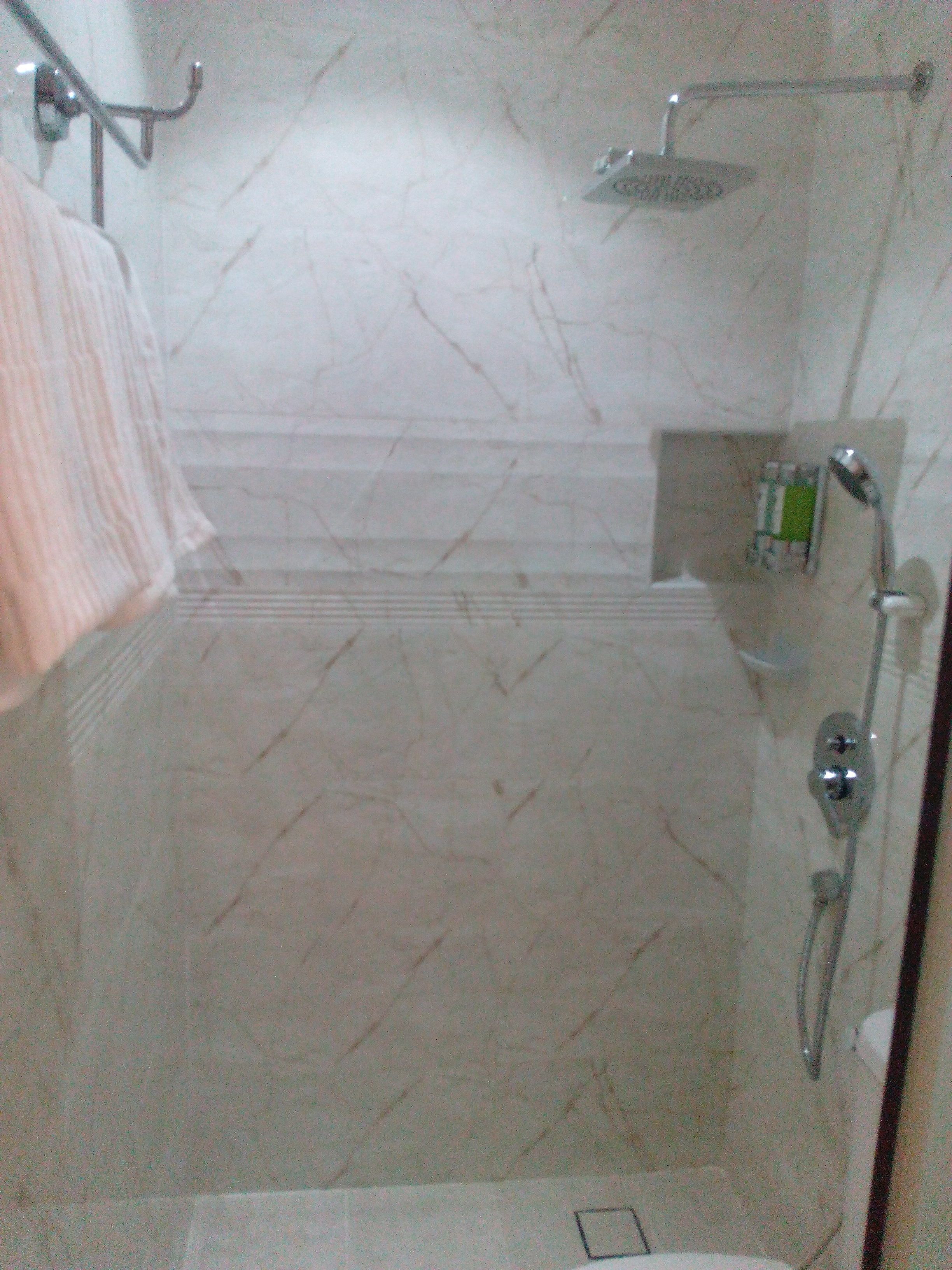 A bathroom with a shower, a towel rack, and a small shelf with toiletries.