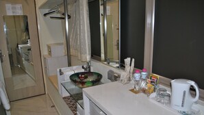 Un baño con un lavabo de vidrio, encimera blanca, espejo y artículos de aseo.