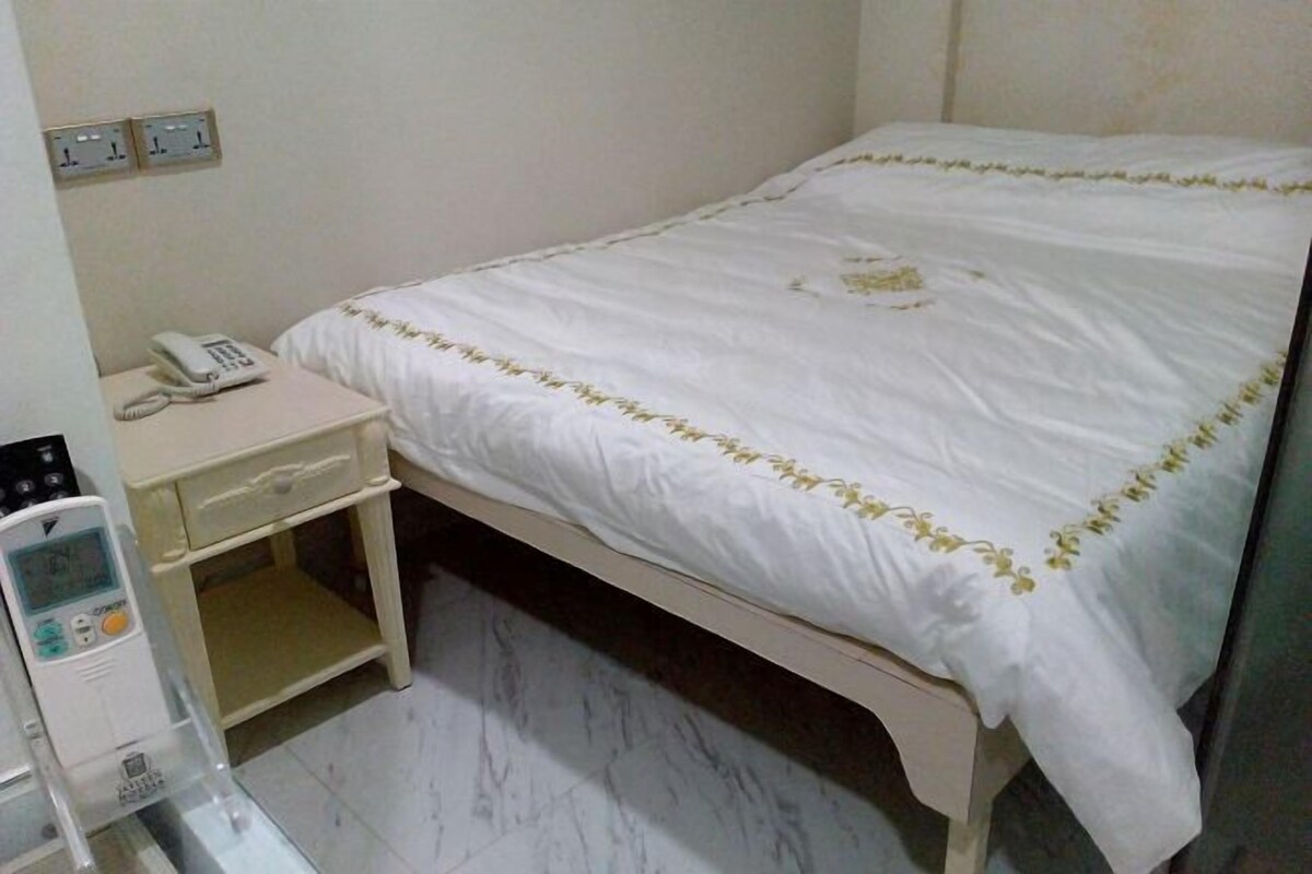 Una camera d'hotel con un letto, un comodino e una piccola scrivania con un telefono e un dispositivo medico.