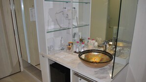 Un baño con cabina de ducha de vidrio, un lavabo y distintos artículos de aseo en la encimera.