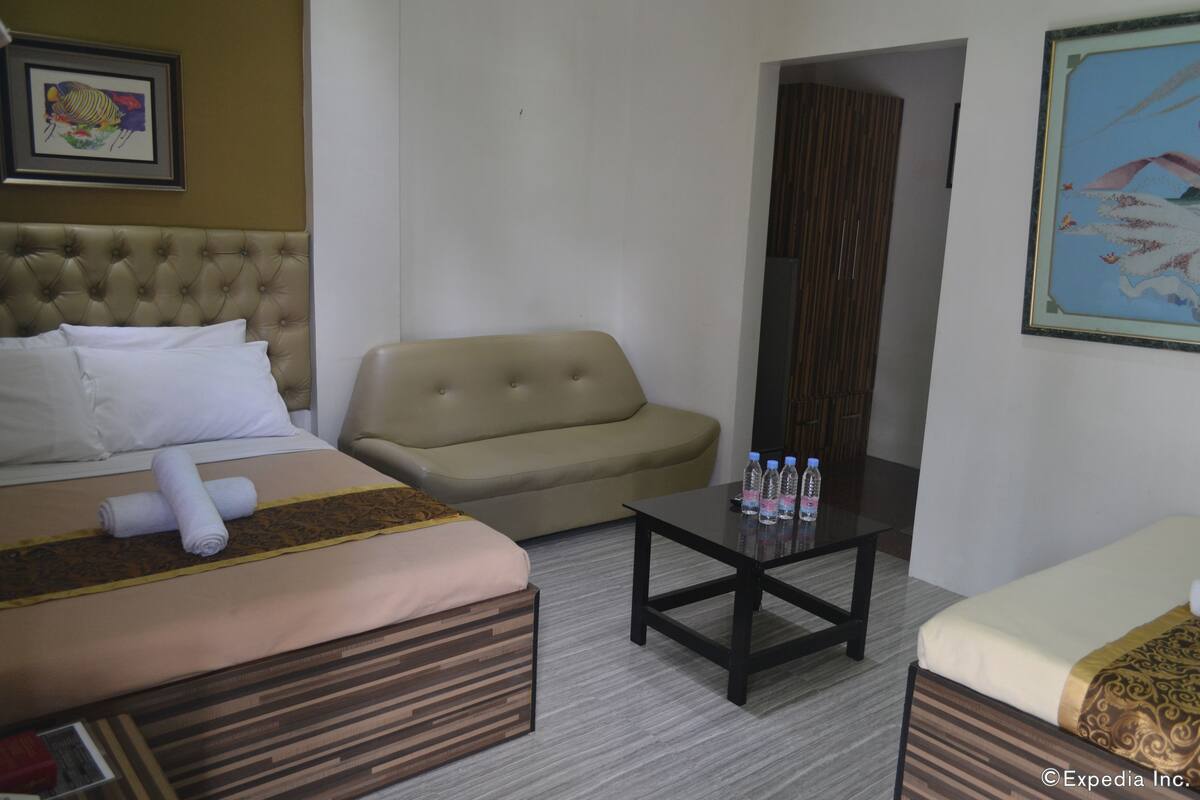 A hotel room with a bed, a sofa, a coffee table, and a painting on the wall.