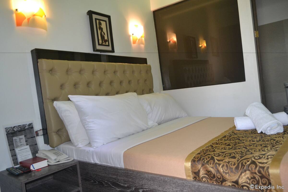 A hotel room with a large bed, a bedside table with a telephone and a book, and wall-mounted lights.