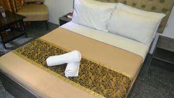 Una cama bien tendida con una colcha estampada, un par de toallas enrolladas y un cabecero con diseño acolchado.