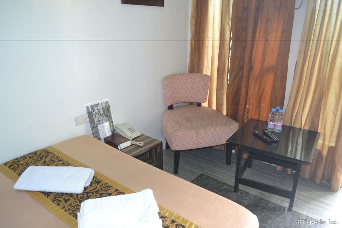 A hotel room with a bed, a chair, a small table, a telephone, and a window with curtains.