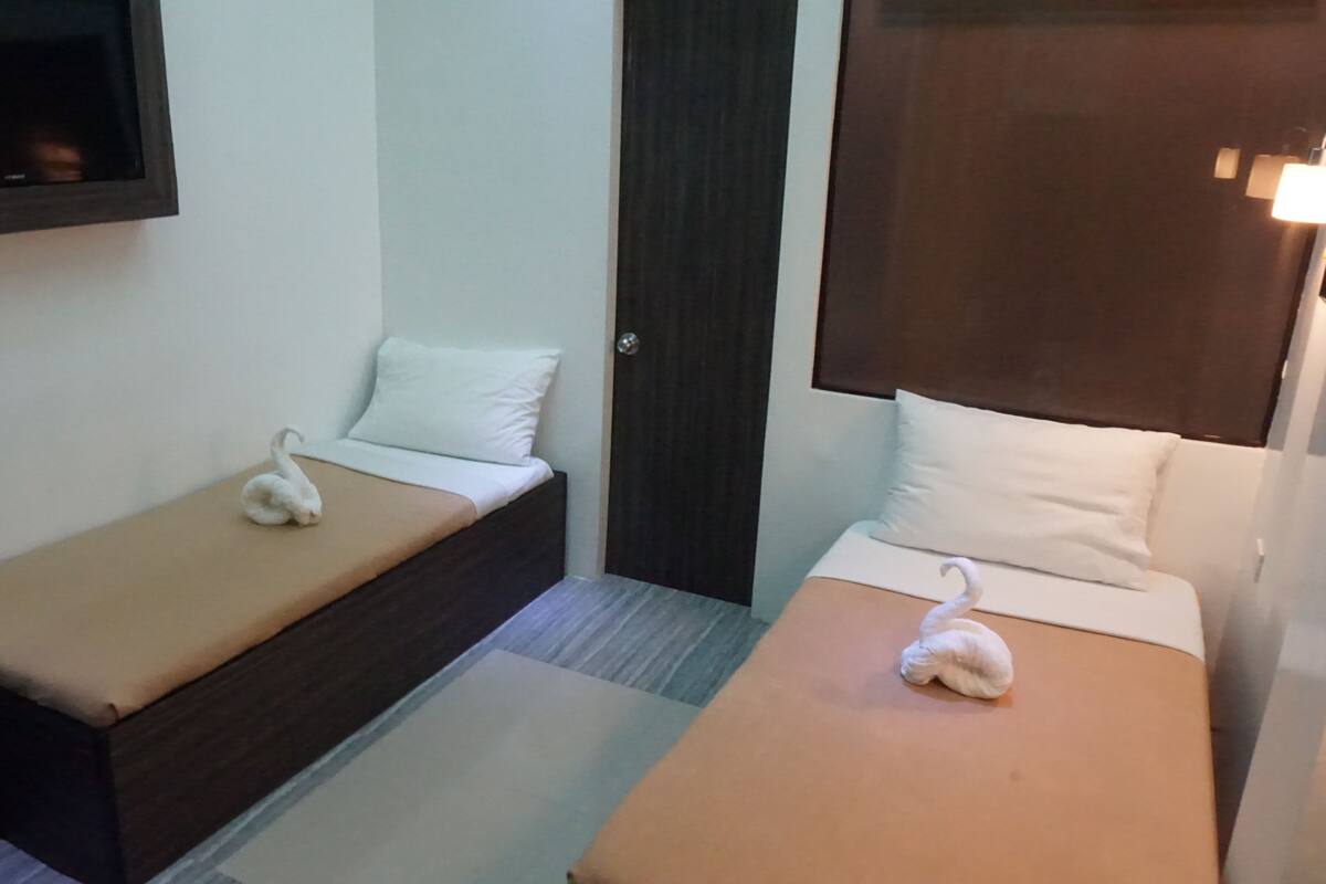 Two single beds with swan-shaped pillows, a small bedside table, and a wall-mounted TV.