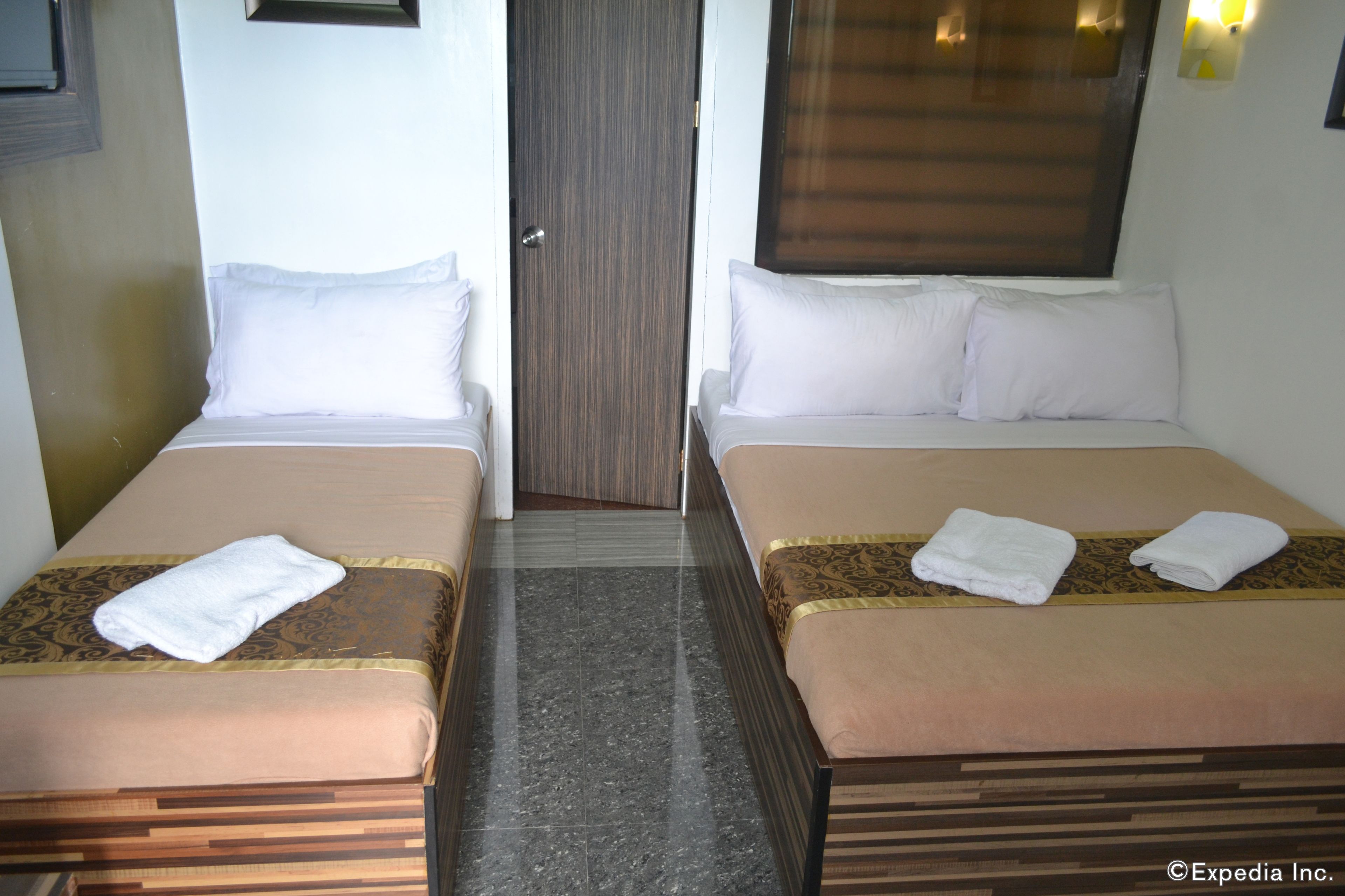 Two single beds with white linens and towels, a wooden floor, and a door in the center.