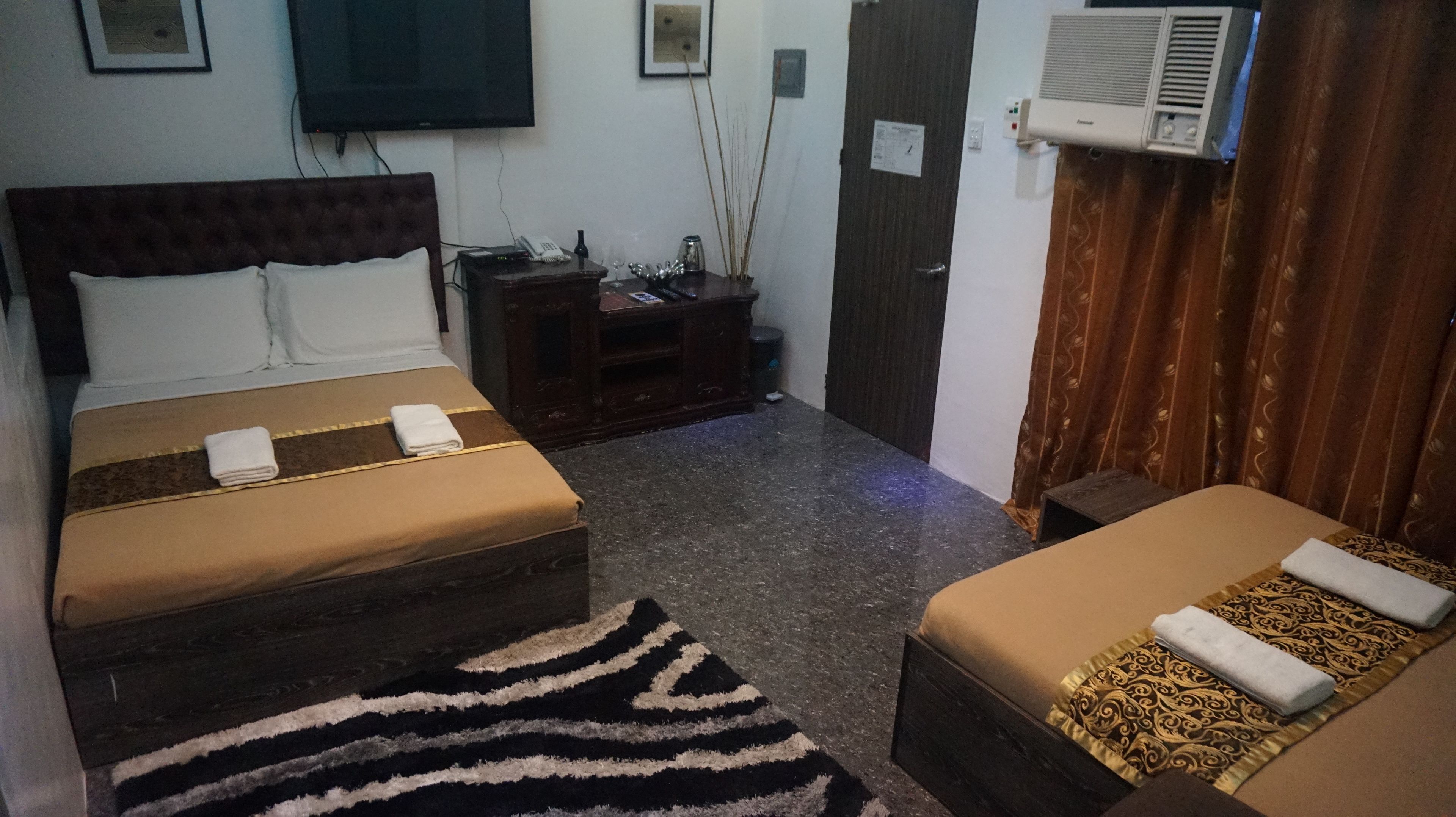 A hotel room with two beds, a TV, a minibar, and a window with curtains.