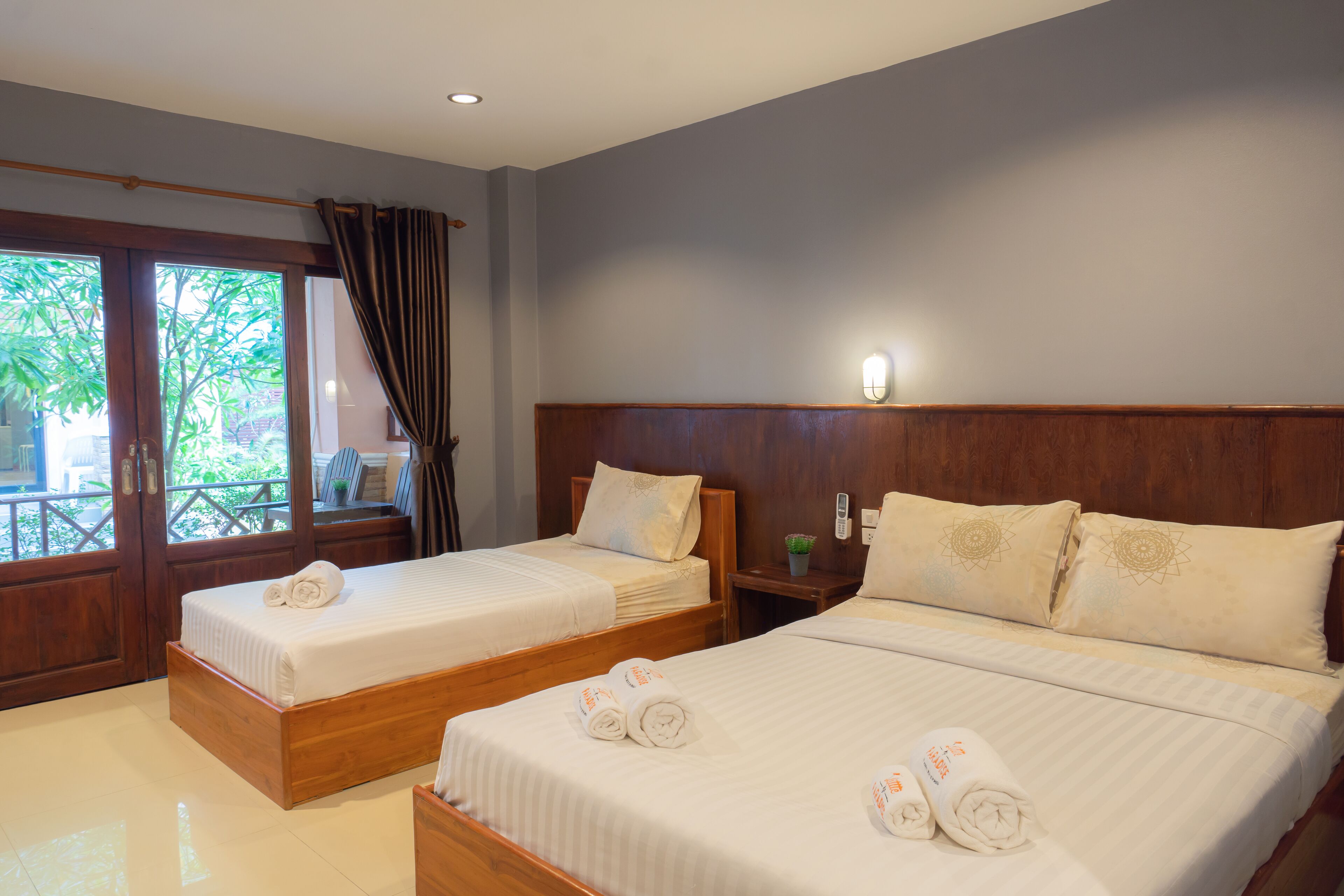 Quarto de hotel com duas camas, cabeceiras de madeira e uma janela grande com cortinas.