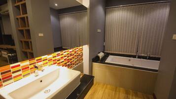 A modern bathroom with a large bathtub, a white sink, and a mirror with a colorful tile backsplash.