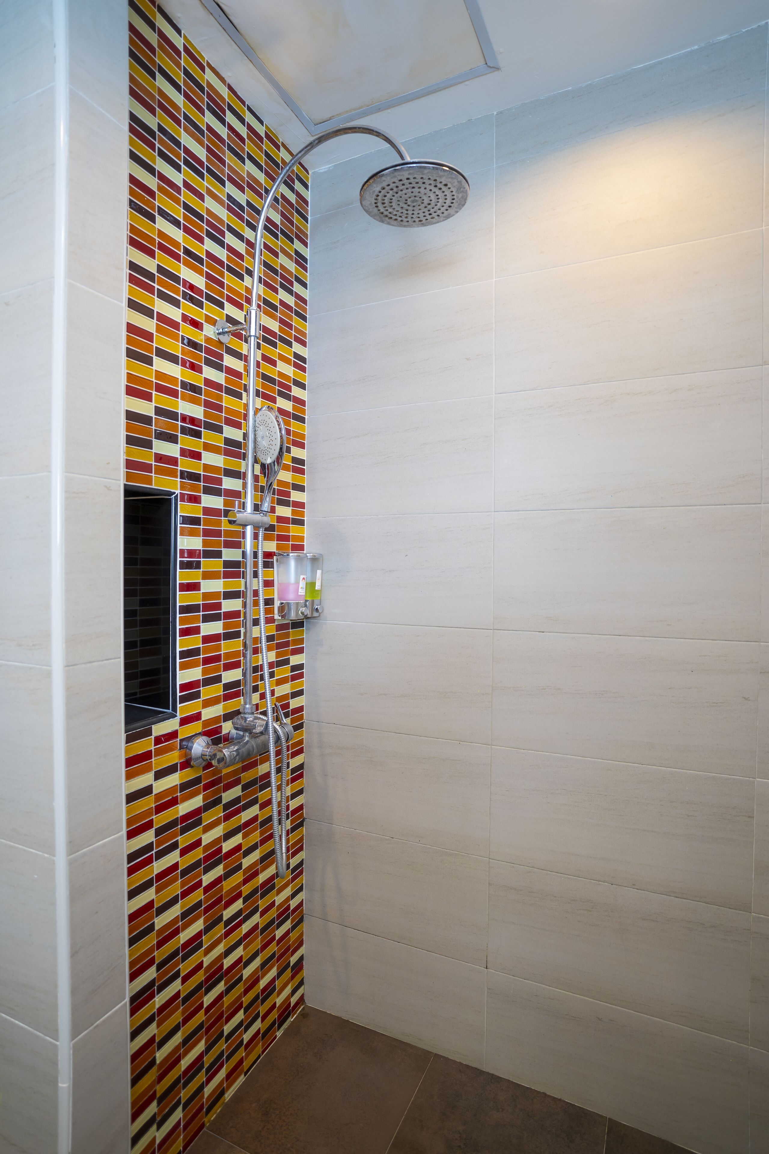 A shower with a colorful mosaic wall, a handheld showerhead, and a wall-mounted faucet.