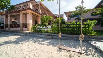 A hotel with a sign reading "Little Paradise" and a swing set in the foreground.
