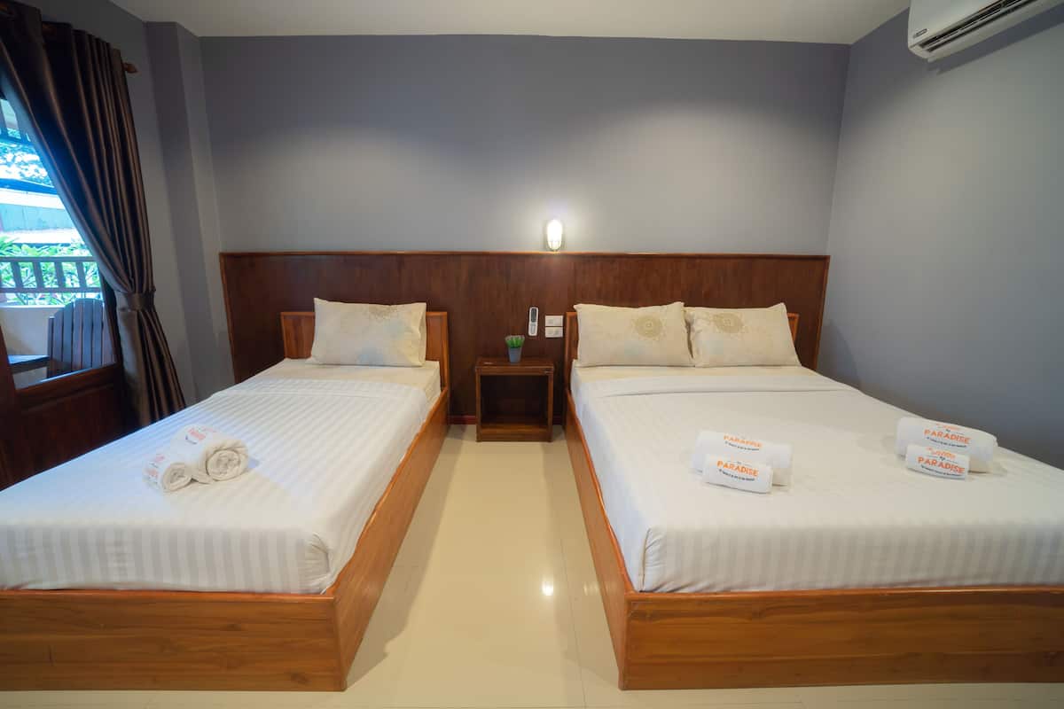 A hotel room with two single beds, wooden headboards, white linens, a nightstand with a remote control, and a window with curtains.