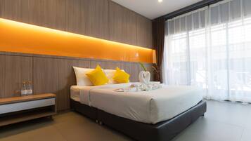 A modern hotel room with a large bed, a bedside table, and a view of the outdoors through sheer curtains.