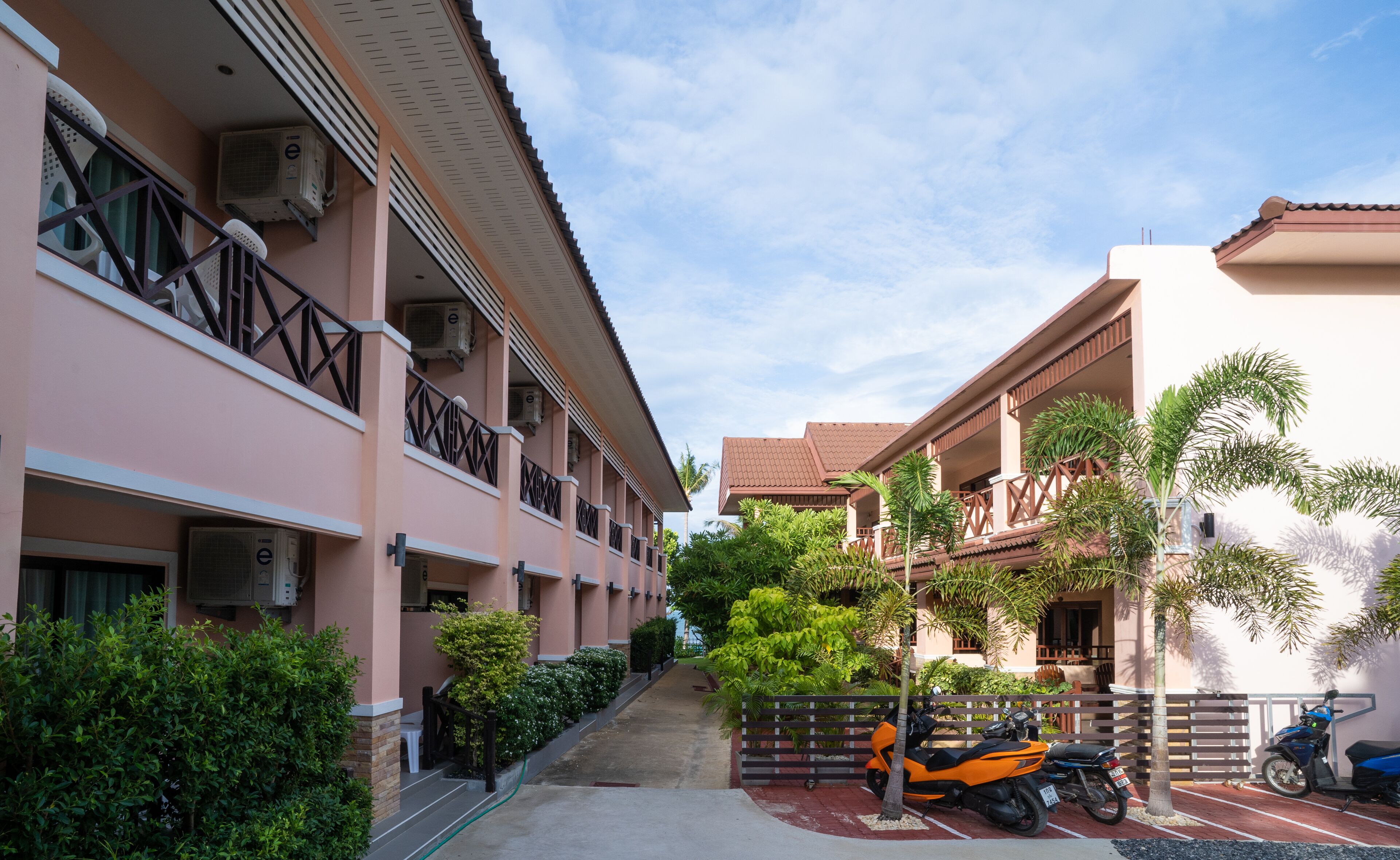 A hotel with a covered walkway, multiple balconies, and parked motorcycles.