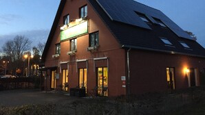 Um edifício de dois andares com telhado inclinado, painéis solares e uma placa indicando um restaurante ou café.