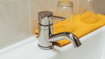 A bathroom sink with a chrome faucet, a yellow towel, and two glass jars in the background.