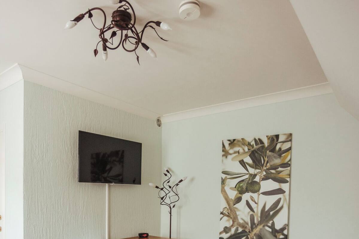 A bedroom with two wooden beds, a desk with a chair, a flat-screen TV, and a ceiling light fixture.
