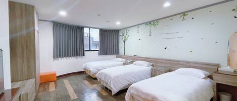 A hotel room with three beds, a wooden floor, a window with curtains, and a wall with a nature-themed design.