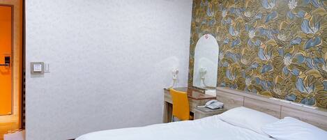 A hotel room with a bed, a bedside table with a phone, a mirror, and a floral wallpaper.