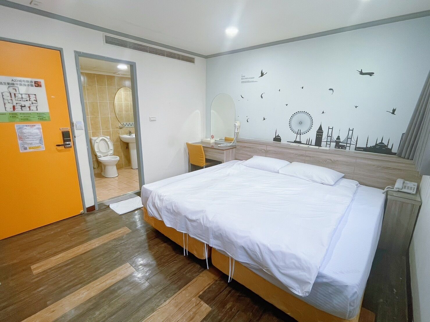 A hotel room with a bed, a nightstand, a mirror, and a wall with cityscape decals.